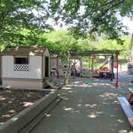 The pathway between the play area next to the pool and the play area next to Discovery Building. On the left is a playhouse and straight ahead is the area where the trikes and bikes and play cars are stored. Beyond this storage area is the Persimmon orchard.